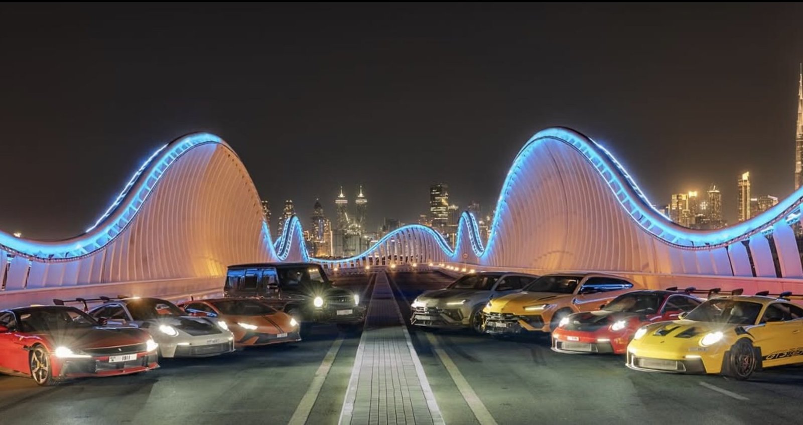 YAZ Car Rental fleet of Ferrari, Porsche, Lamborghini and Mercedes-AMG vehicles lined up at night on a Dubai bridge